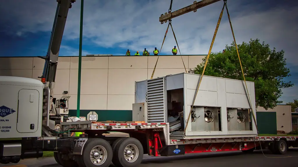 A crane lifting a large packaged rooftop unit off a flatbed at a commercial job