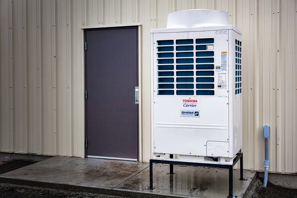 A Toshiba-Carrier outdoor unit installed on a level stand beside a service door